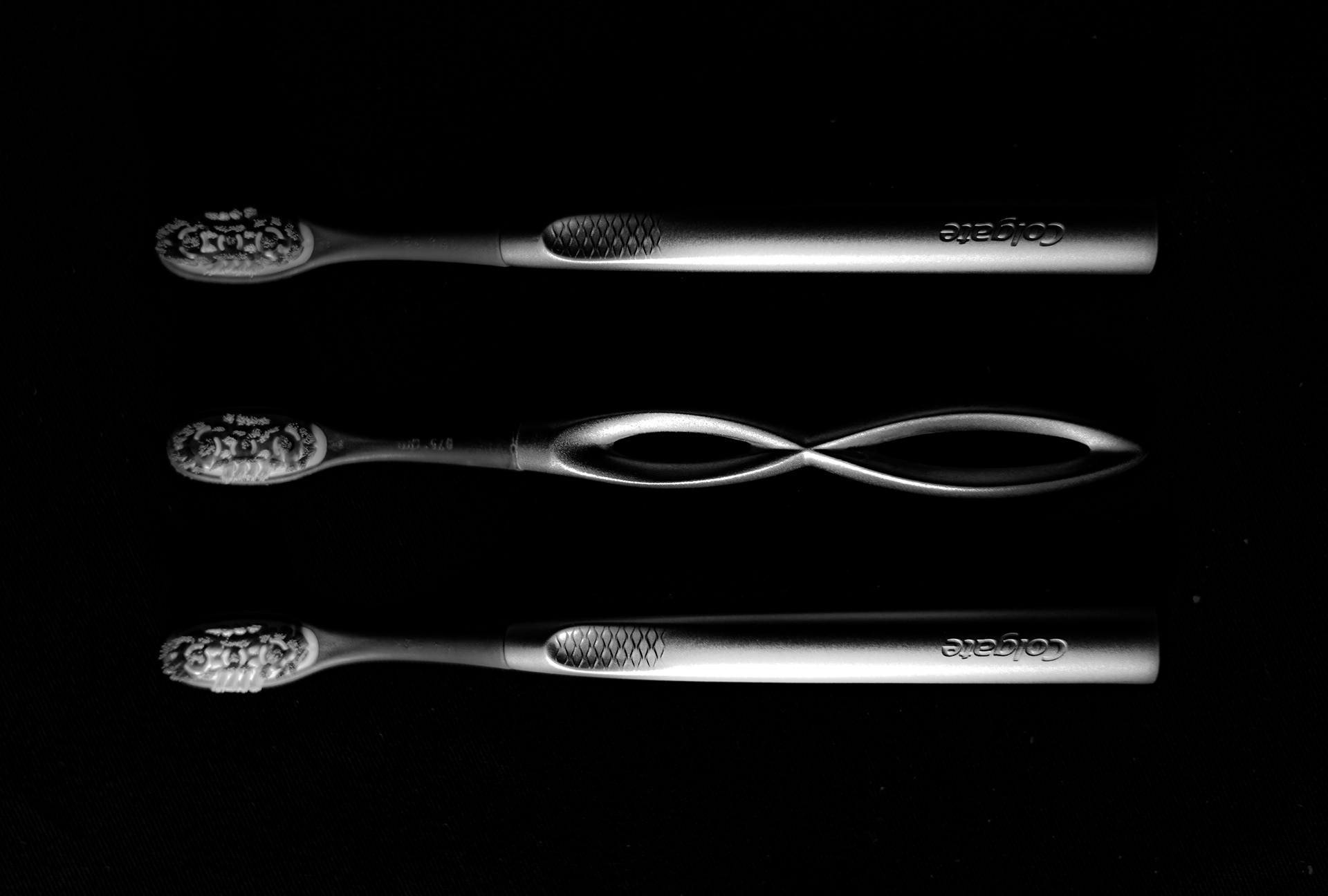 Three metal toothbrush in a column, the middle toothbrush has an infinity shaped handle.