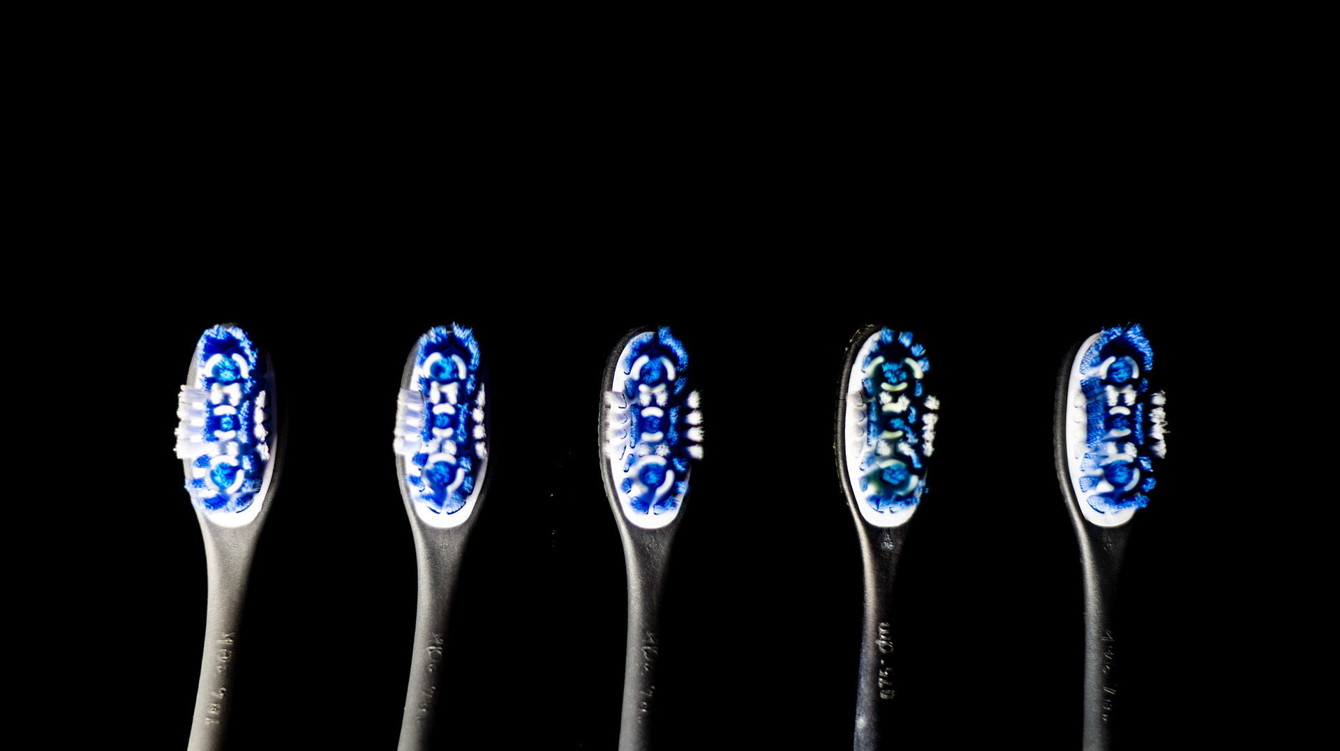 a close up shot of five toothbrush heads in the bottom half of the frame, lit in a gradient from light to dark.