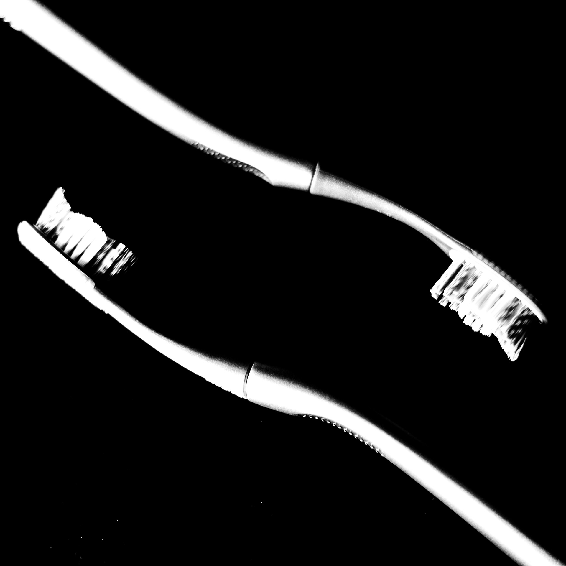 Two toothbrushes are pictured in high contrast black and white reaching past each other from opposite corners of the image.